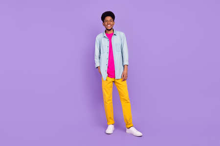 Photo of adorable cute dark skin guy dressed jeans shirt arm pocket smiling isolated violet color backgroundの写真素材