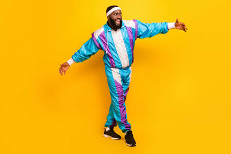 Photo of funny charming dark skin guy dressed sport suit headband smiling dancing walking isolated yellow color backgroundの写真素材
