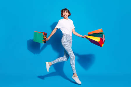 Photo of funny sweet young lady wear white outfit smiling walking holding bargains isolated blue color backgroundの写真素材