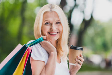 Photo of aged optimistic blond lady hold tea bags wear white t-shirt in park aloneの写真素材