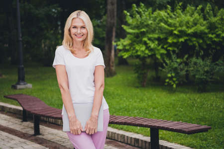 Photo of mature business blond lady hold laptop wear white t-shirt in park aloneの写真素材