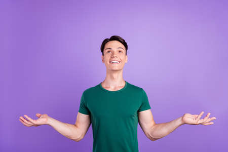 Photo of cheerful positive young man raise hands empty space look up enjoy isolated on violet color backgroundの写真素材