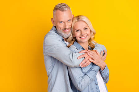 Photo of cheerful joyful happy old couple hug embrace care enjoy harmony hands isolated on yellow color backgroundの写真素材