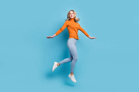 Full length photo of cheerful young woman look empty space jump up air isolated on pastel blue color backgroundの写真素材