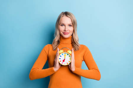 Photo of cheerful young happy woman hold hands alarm clock smile hour isolated on blue color backgroundの写真素材