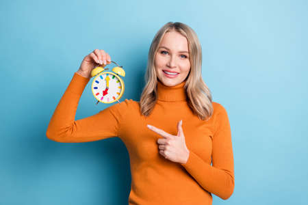 Photo of positive young woman point finger alarm clock time management isolated on blue color...