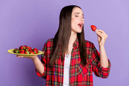 Photo of nice brunette hairdo young lady eat fruit wear red shirt isolated on purple color backgroundの写真素材