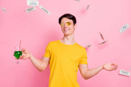 Photo of young guy happy positive smile drink cocktail fly air fall money cash dollars rich isolated over pastel color backgroundの写真素材