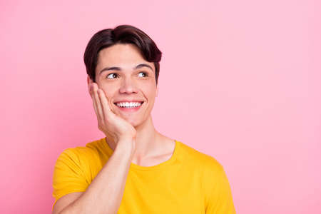 Photo of cute charming young guy dressed yellow t-shirt arm cheek looking empty space smiling isolated pink color backgroundの写真素材