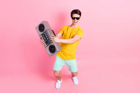 Photo of funky crazy cool guy dance hold boombox wear sunglass yellow t-shirt shorts isolated on pink backgroundの写真素材