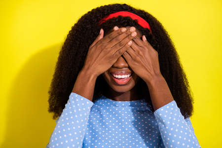 Photo portrait of curly girl smiling covering eyes with hands isolated on vivid yellow color backgroundの写真素材