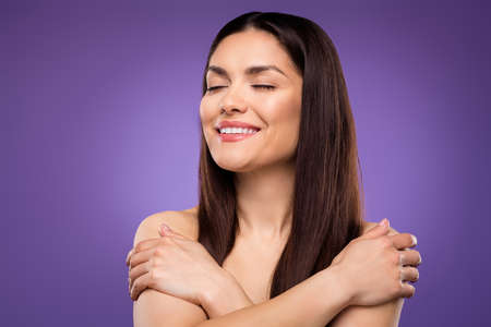 Portrait of attractive dreamy cheerful woman hugging herself enjoying isolated over bright violet purple color backgroundの写真素材