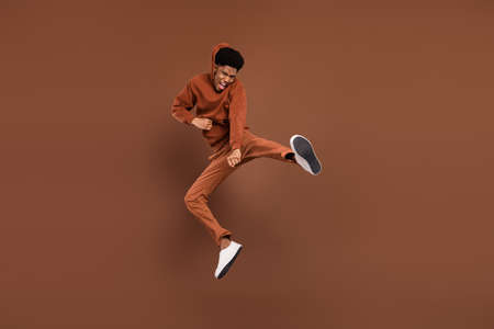 Photo of funky strong dark skin man wear sweatshirt smiling jumping high practicing karate isolated brown color backgroundの写真素材