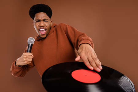 Photo of joyful short hairdo millennial guy play disc sing in mic dress sportswear isolated on brown color backgroundの写真素材
