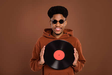 Photo of funny brunet hairdo millennial guy hold disc dress spectacles sportswear isolated on brown color backgroundの写真素材