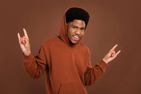 Photo of cool brunet hairdo millennial guy show rock sign dress sportswear isolated on brown color backgroundの写真素材