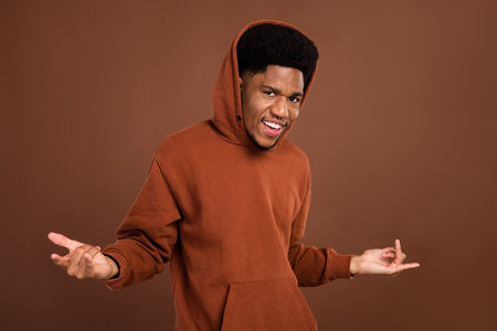 Photo of young black guy happy positive smile show finger horns rock sign music lover isolated over brown color backgroundの写真素材