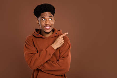 Photo of optimistic brunet hairdo young guy point empty space dress sportswear isolated on brown color backgroundの写真素材