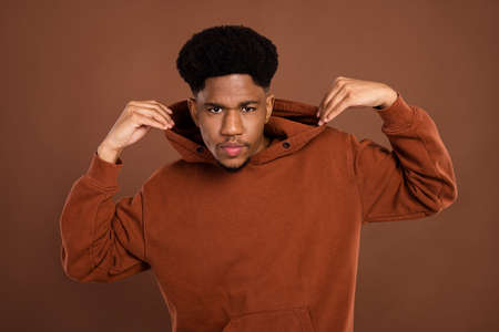 Photo of young handsome afro guy hands touch hood jumper serious narcissistic isolated over brown color backgroundの写真素材