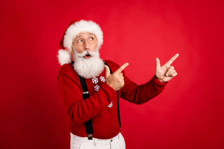 Photo of aged man wear santa hat amazed point fingers empty space ad promo direct select isolated over red color backgroundの写真素材