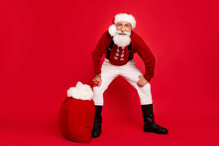 Full size photo of santa claus happy positive smile carry bag gift rest eve time tradition isolated over red color backgroundの写真素材