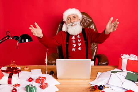 Photo of santa claus happy positive smile open arms glad hug welcome sit table laptop isolated over red color backgroundの写真素材