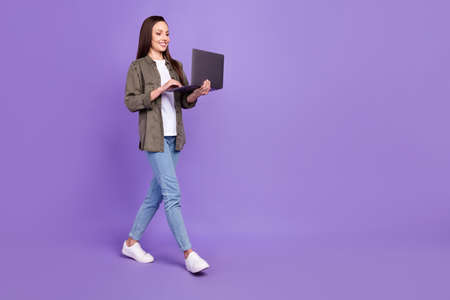 Full size profile side photo of smiling businesswoman receive email in laptop go walk isolated on purple color backgroundの写真素材