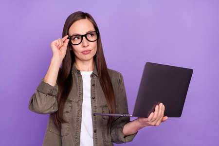 Photo of beautiful mature serious businesswoman look copyspace thinking hold computer isolated on purple color backgroundの写真素材