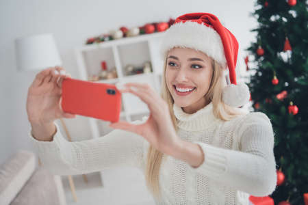 Photo of cute adorable young lady wear knitted pullover smiling tacking selfie modern device indoors house home roomの写真素材