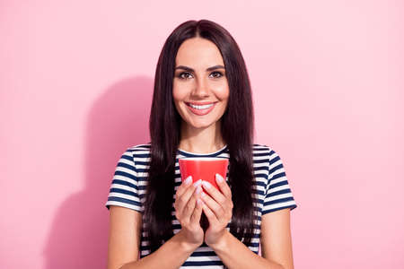 Portrait of attractive long-haired cheerful girl drinking beverage isolated over pink pastel color backgroundの写真素材