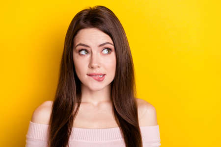 Photo of shy brunette lady bite lips look empty space wear pink shirt isolated on yellow color backgroundの写真素材