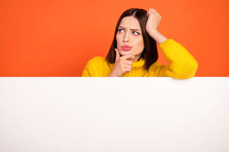 Photo of young woman hand touch chin think look empty space advert information isolated over orange color backgroundの写真素材