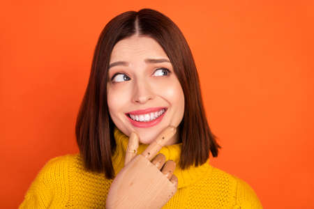 Photo of young woman happy smile hand touch chin prosthesis handicapped think look empty space isolated over orange color backgroundの写真素材