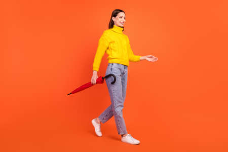 Full size profile side photo of young woman happy positive smile go walk wet forecast umbrella isolated over orange color backgroundの写真素材