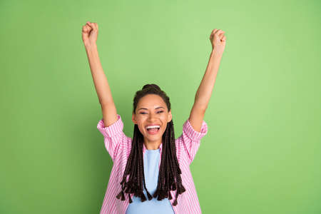 Photo of young cheerful dark skin woman raise fists winner celebrate isolated on shin green color backgroundの写真素材