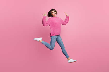 Full length photo of cheerful young happy positive woman jump up enjoy weekend isolated on pink color backgroundの写真素材