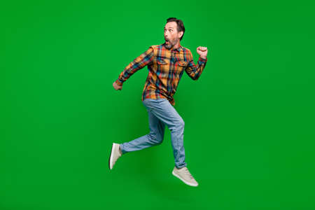 Full length body size view of attractive funky amazed man jumping running away isolated over bright green color backgroundの写真素材