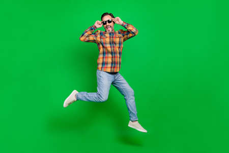 Full length body size view of nice cheerful man jumping touching specs having fun isolated over bright green color backgroundの写真素材