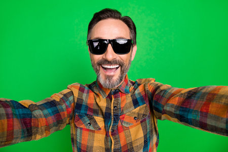 Self-portrait of attractive cheerful man wearing specs having fun isolated over bright green color backgroundの写真素材