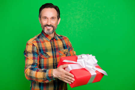 Portrait of attractive cheerful man holding in hands festal romantic giftbox isolated over bright green color backgroundの写真素材