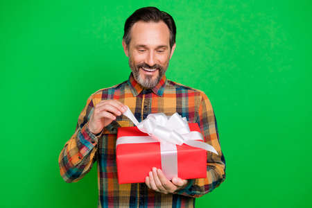 Portrait of attractive cheerful man holding in hands opening festal giftbox isolated over bright green color backgroundの写真素材
