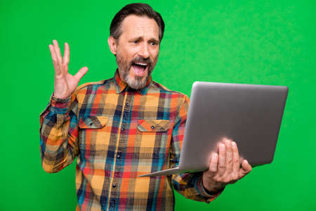 Portrait of attractive worried man using laptop reading finance report fail isolated over bright green color backgroundの写真素材