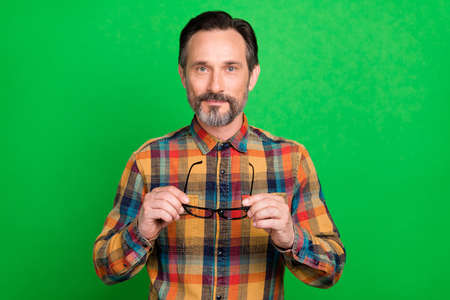 Portrait of attractive bearded guy wearing checked shirt holding in hands eyewear isolated over bright green color backgroundの写真素材