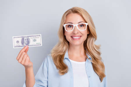Photo of cheerful candid lady hold dollar promote bank service wear specs blue shirt isolated grey color backgroundの写真素材