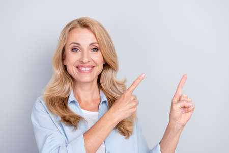 Portrait of cheerful beautiful young woman point fingers copyspace advertising product isolated on grey color backgroundの写真素材