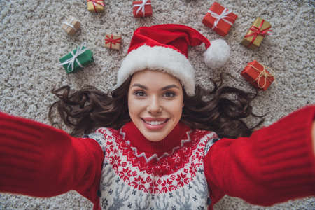 Top view photo portrait smiling woman wearing headwear laying on floor in xmas clothes taking selfieの写真素材
