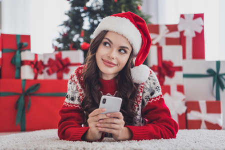 Photo of blogger lady lay carpet texting phone look up wear santa hat sweater in decorated home indoorsの写真素材