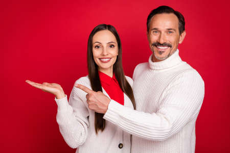 Photo of attractive husband wife couple point finger empty space hold hand object xmas isolated on red color backgroundの写真素材
