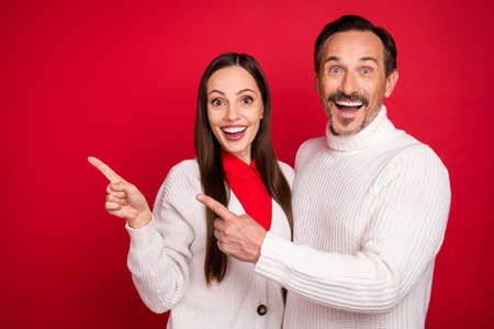 Photo of amazed cheerful man and woman husband wife point finger empty space sale news isolated on red color backgroundの写真素材