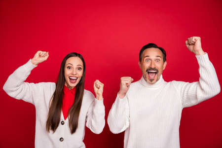 Photo of cheerful amazed happy mature man and woman winner raise hands isolated on red color backgroundの写真素材